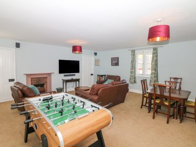 A living room with a foosball table brown leather sofas a dining table with chairs and a wall-mounted television at Crablake Farmhouse in Exminster