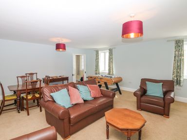 A living room with brown leather sofas a wooden coffee table a dining table with chairs and a foosball table at Crablake Farmhouse in Exminster