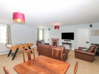 A living room with leather sofas a foosball table a wooden dining table and a TV on the wall at Crablake Farmhouse in Exminster