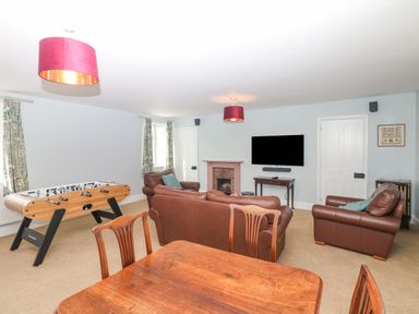 A living room with brown leather sofas a foosball table a wooden dining table a flat screen TV and a fireplace at Crablake Farmhouse in Exminster