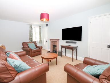 A living room with brown leather sofas a wall-mounted television a wooden coffee table and a fireplace at Crablake Farmhouse in Exminster