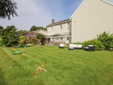A garden with outdoor furniture a croquet set and a swing next to a house at Crablake Farmhouse in Exminster