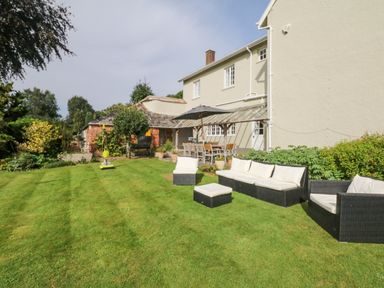 A backyard with wicker outdoor furniture and a dining table with chairs under an umbrella at Crablake Farmhouse in Exminster
