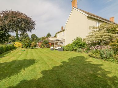 A garden with lawn chairs and a table next to a large house with bushes and trees at Crablake Farmhouse in Exminster