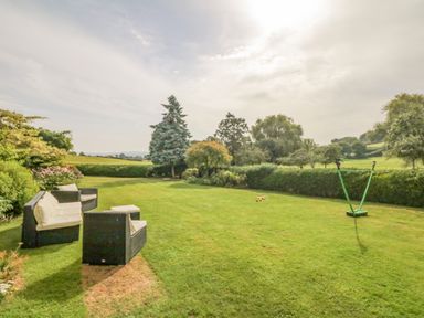 An outdoor garden with lawn chairs and a badminton net at Crablake Farmhouse in Exminster