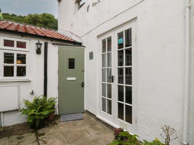 An outdoor corner with a green door a white double glass door potted plants and a small lantern light at The Nook in Whitby