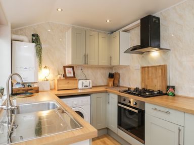 A kitchen with wooden countertops a sink a gas stove an oven cabinets a washing machine and kitchen appliances at The Nook in Whitby