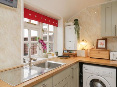 A kitchen sink under a window with red blind and a washing machine under wooden countertops at The Nook in Whitby
