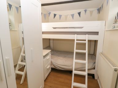A small bedroom with a white bunk bed a ladder a white wardrobe and a small white chest of drawers at The Nook in Whitby