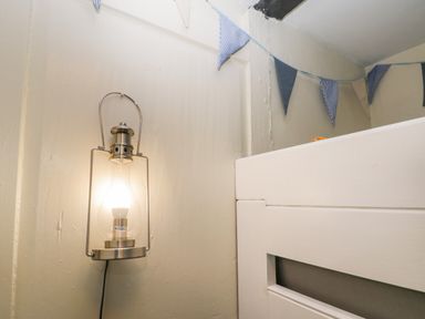A lit wall-mounted lamp next to a white wooden bed frame with blue and white bunting above at The Nook in Whitby