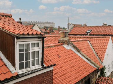 A view of red tiled rooftops with chimneys and windows under a partly cloudy sky at The Nook in Whitby