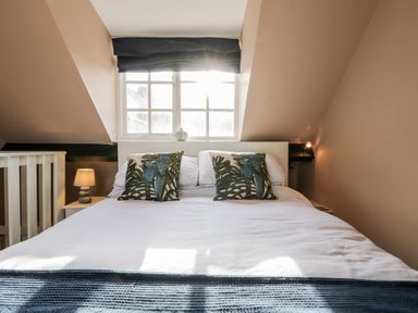 A bedroom with a white bed and bird patterned pillows under a window with black curtains at The Nook Whitby