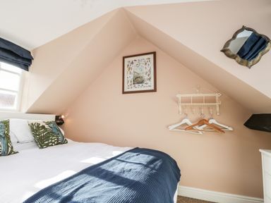 A bedroom with a bed with white sheets and decorative pillows near a window and wall hangers with clothes hangers at The Nook in Whitby
