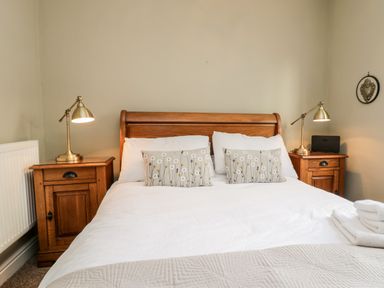 A bedroom with a wooden bed frame two bedside tables with lamps and pillows with flower designs at The Nook in Whitby