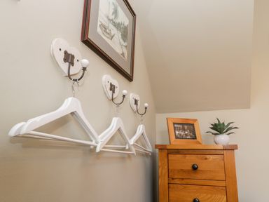 A corner with white hangers on wall hooks and a wooden chest with a potted plant and framed photo at The Nook in Whitby