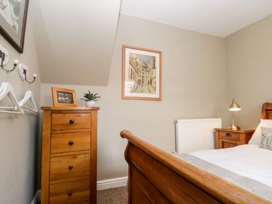 A bedroom with a wooden bed, bedside table with lamp, chest of drawers, framed pictures, and hangers on the wall at The Nook in Whitby