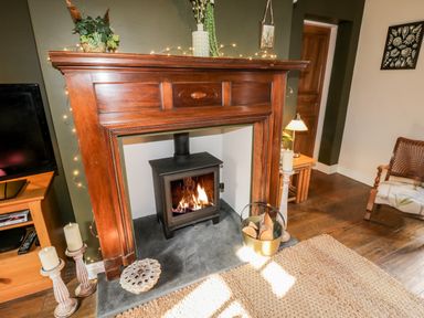 A living room with a wood burning stove in a wooden fireplace a bucket with firewood and candles at The Nook in Whitby