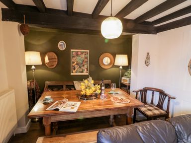 A dining room with a wooden table set with a magazine wine bottle cups and food with a bench and chairs against a green wall with lamps and mirrors at The Nook in Whitby