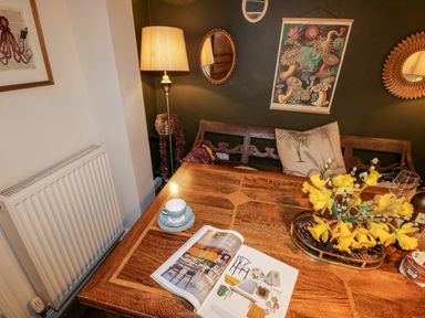 A wooden dining table with a magazine a cup and saucer and a vase with yellow flowers against a dark wall with mirrors and framed art at The Nook in Whitby