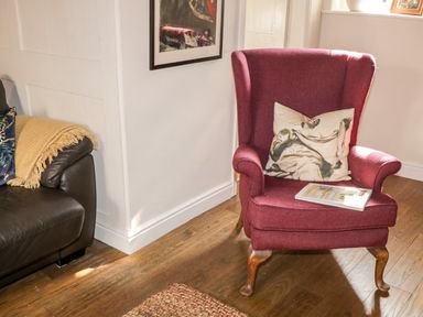 A red armchair with a printed cushion and a book on it next to a black leather couch with a yellow throw in a room at The Nook in Whitby