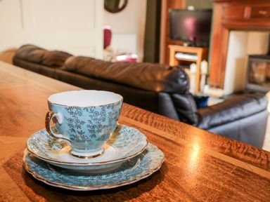 A blue floral teacup and saucers on a wooden table with a black sofa and television in the background at The Nook in Whitby