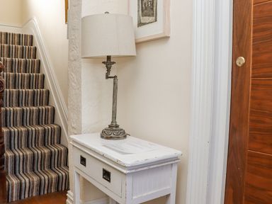 A striped carpeted staircase next to a white wooden side table with a lamp and papers on it at Heron in St Ives