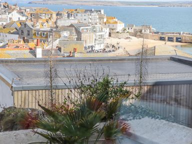 View of rooftops by the sea with people on a beach and a stone pier at Heron in St Ives
