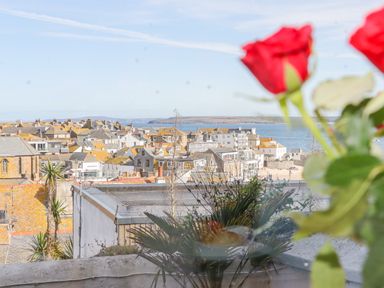 A view of rooftops and buildings with the sea in the background and red flowers in the foreground at Heron in St Ives