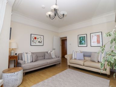 A living room with two sofas, cushions, framed artwork on walls, a side table with lamp, a patterned rug, and a plant at Whistler in St Ives