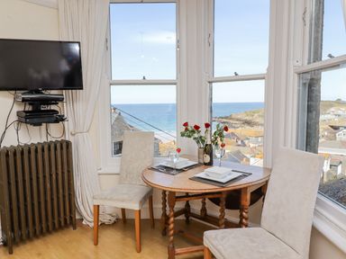 A small dining area with two chairs and a round wooden table set with plates glasses and a bottle of champagne by a window overlooking the sea at Whistler in St Ives
