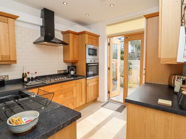 A kitchen with wooden cabinets black countertops a gas stove an oven a dishwasher dish rack a door leading outside at Whistler in St Ives