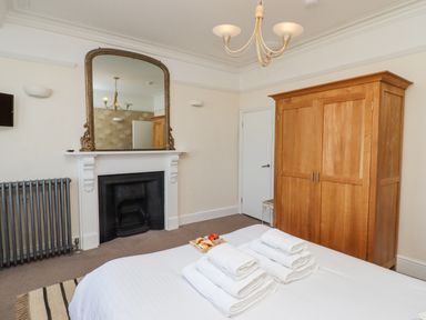 A bedroom with a bed and folded towels next to a wooden wardrobe and a fireplace with a mirror above it at Whistler in St Ives