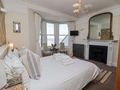 A bedroom with a bed towels on it two chairs and a table near windows and a fireplace with a mirror above at Whistler in St Ives