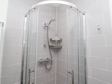 A corner shower with glass sliding doors and a handheld showerhead in a tiled bathroom at Whistler in St Ives