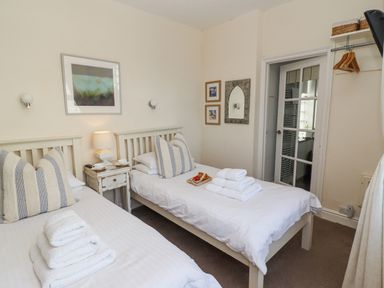 A bedroom with two single beds striped pillows a nightstand with lamp and door leading to bathroom at Whistler in St Ives