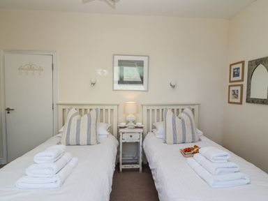 A bedroom with two single beds with striped pillows and folded towels with a nightstand and lamp between at Whistler in St Ives