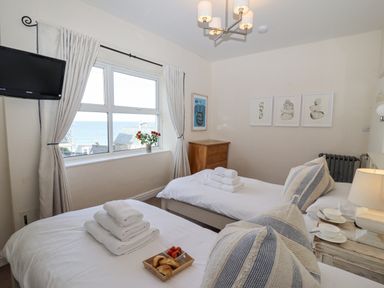 A bedroom with two single beds a chest of drawers and a window overlooking the sea at Whistler in St Ives