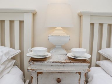 A bedside table with a lamp two white cups and saucers between two beds at Whistler in St Ives