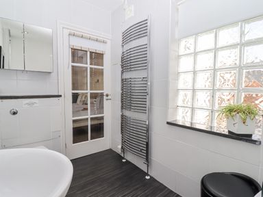 A bathroom with a white sink a chrome heated towel rail a glass block window and a door with glass panels at Whistler in St Ives