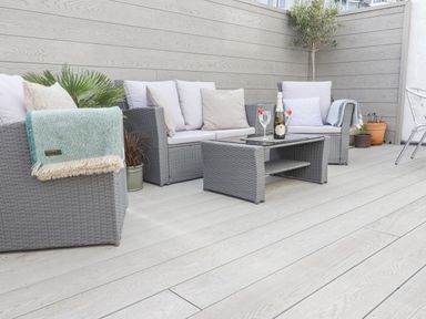 An outdoor patio with grey wicker seating cushions a coffee table and potted plants at Whistler in St Ives