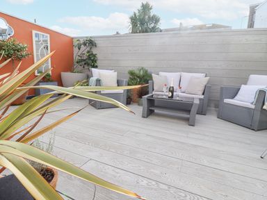 An outdoor seating area with grey wicker chairs and a sofa around a glass table on a wooden deck at Whistler in St Ives