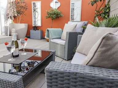 A patio seating area with grey wicker chairs and a table with wine glasses and a bottle in Whistler in St Ives