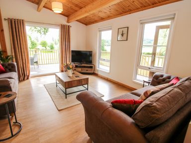 A living room with two sofas a coffee table a television and sliding doors leading to a balcony at The Log Cabin in Newnham Bridge near Tenbury Wells