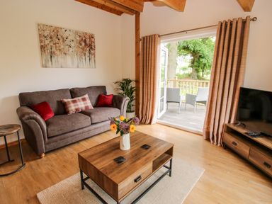 A living room with a sofa and coffee table opening onto a wooden balcony with chairs at The Log Cabin in Newnham Bridge near Tenbury Wells