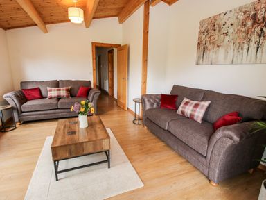A living room with two brown sofas red and plaid cushions a wooden coffee table with flowers and wooden ceiling beams at The Log Cabin in Newnham Bridge near Tenbury Wells