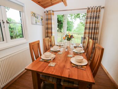 A dining room with wooden table and chairs set with plates bowls and glasses near window and glass door at The Log Cabin in Newnham Bridge near Tenbury Wells