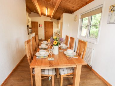 A dining room with a wooden table set for six people next to a kitchen at The Log Cabin in Newnham Bridge near Tenbury Wells