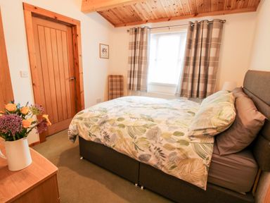 A bedroom with a double bed a wooden door a window with curtains and a vase of flowers on a dresser at The Log Cabin in Newnham Bridge near Tenbury Wells
