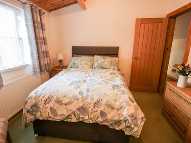 A bedroom with a bed with floral bedding a bedside table with a lamp a wooden door and a dresser with flowers at The Log Cabin in Newnham Bridge near Tenbury Wells