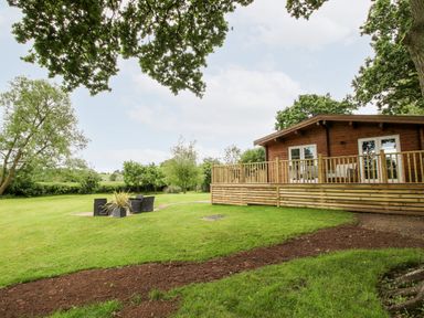 A wooden cabin with a deck and outdoor seating on a grassy lawn at The Log Cabin in Newnham Bridge near Tenbury Wells